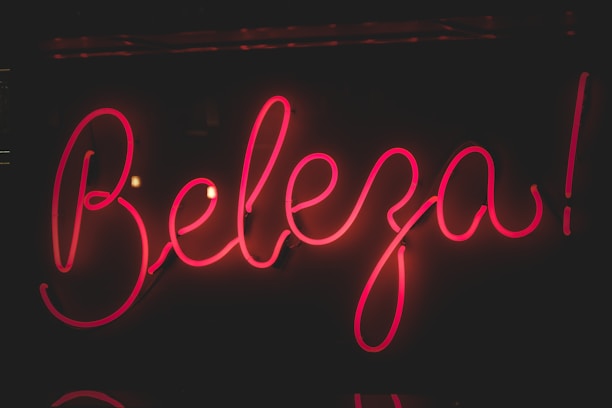 Bright pink neon sign displaying the word 'Beleza' against a dark background. The glowing letters have a cursive style, creating an eye-catching and lively appearance.
