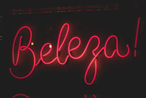 Close-up of a business sign with the name 'brilho copacabana' lit warmly at dusk.