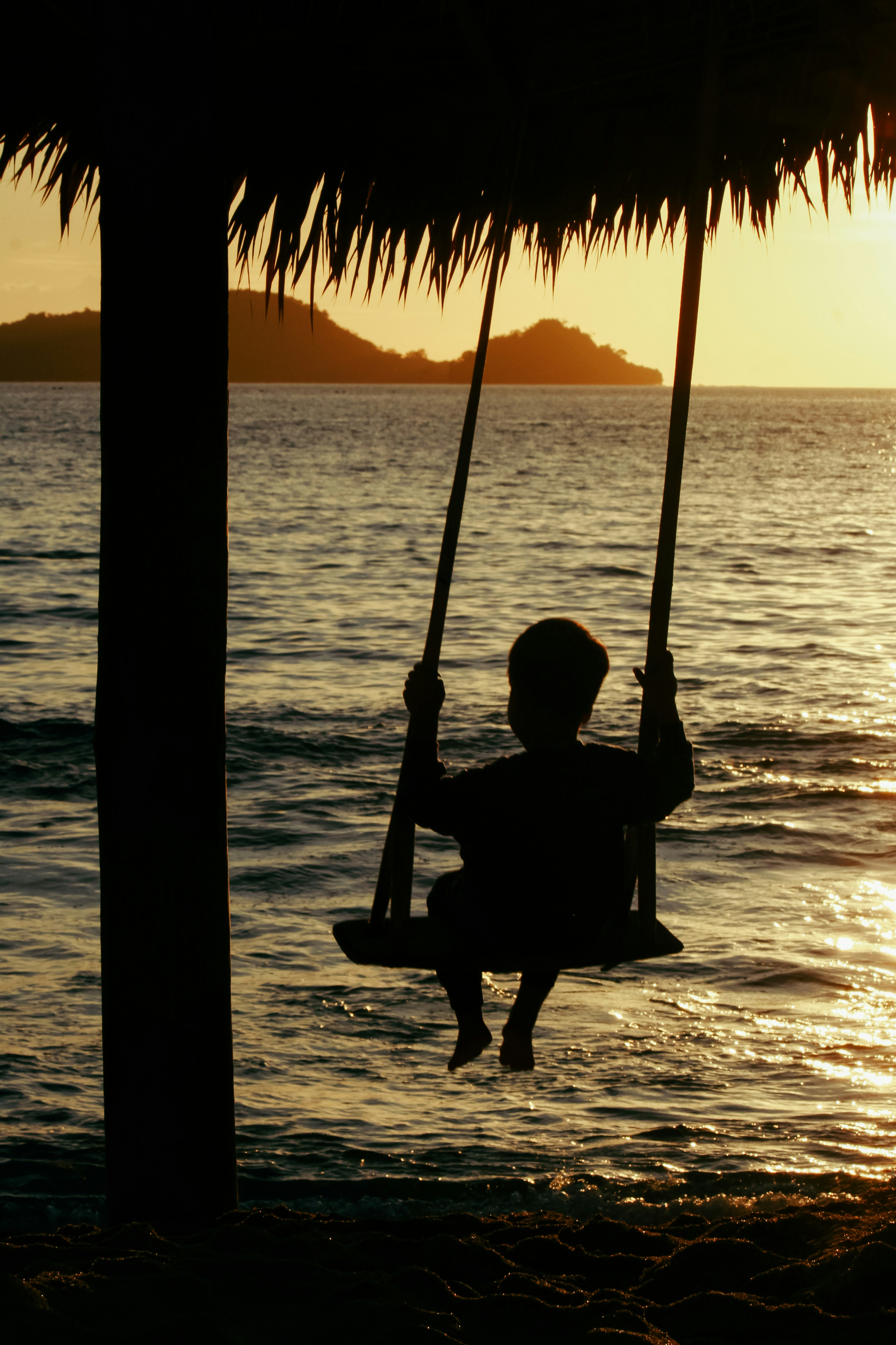 a silhouette of a child on a swing at sunset