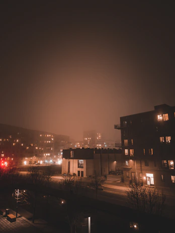 A wide cinematic shot of Brooklyn streets at night, empty except for subtle fog and the faint glow of distant streetlights.