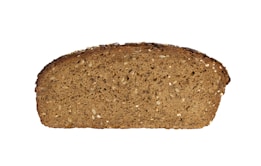 A slice of brown bread filled with visible seeds and grains, featuring a rough, textured surface. The loaf is dense with a dark crust and lighter interior.