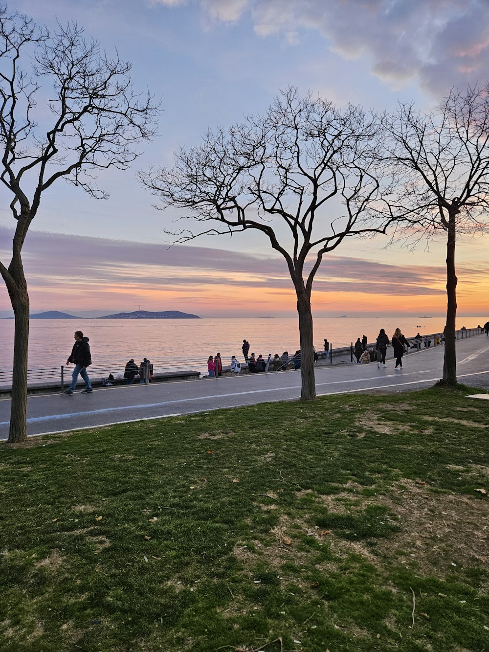 a group of people walking down a sidewalk next to a body of water