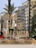 Large illuminated sign reading 'Gran Fira de Valencia' stands prominently in an urban setting surrounded by palm trees and multistory buildings. The sign features vintage-style light bulbs and is situated near a busy street with parked cars and a red bus in the background.