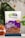 A clear plastic bag containing California almonds is prominently displayed against a blurred background with greenery. The packaging includes branding with the logo '82fit feeding india by zomato' and a purple design with health benefits and 'premium quality' label. A bowl filled with almonds is partially visible on the left.