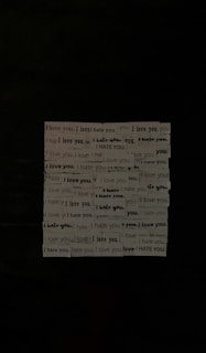 A series of phrases printed on strips of paper, repeatedly alternating between 'I love you' and 'I hate you.' The strips are arranged in a grid-like formation against a dark background, creating a stark visual contrast.