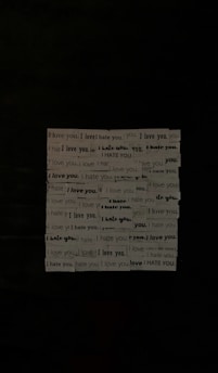 A series of phrases printed on strips of paper, repeatedly alternating between 'I love you' and 'I hate you.' The strips are arranged in a grid-like formation against a dark background, creating a stark visual contrast.
