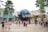 A large globe structure with the letters 'UNIVE' visible, surrounded by a crowd of people taking photos and walking around. The area is lush with palm trees and modern architectural elements, possibly in an amusement or theme park setting.