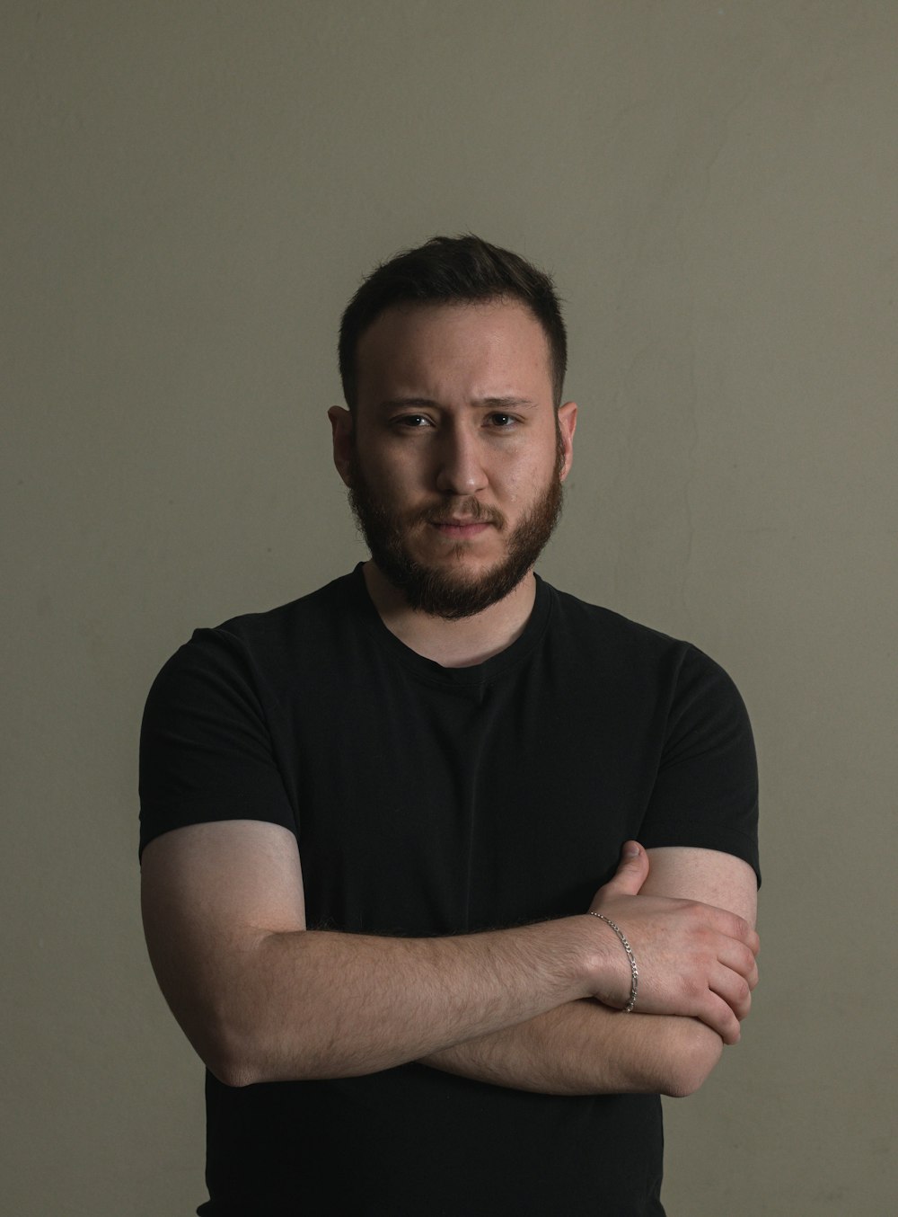 a man with his arms crossed standing in front of a wall