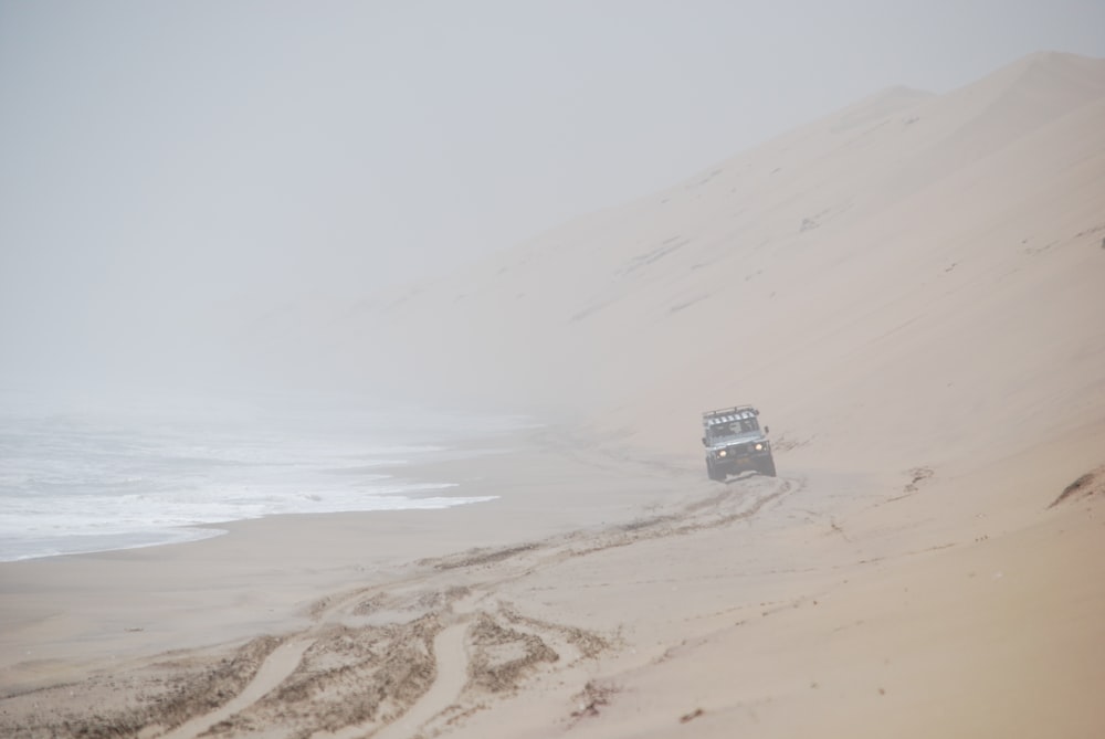 a truck driving down a sandy beach next to the ocean