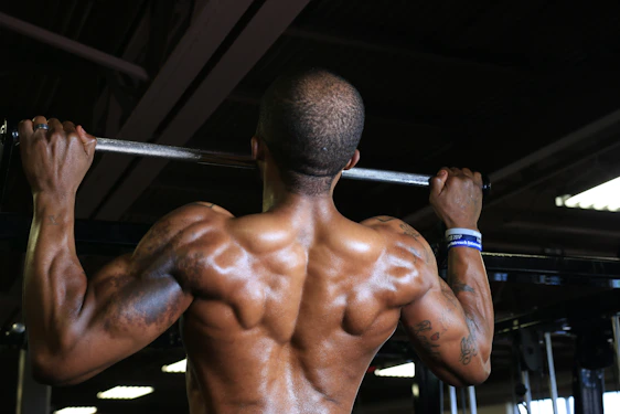An athlete performing a controlled pull-up against a dark gym backdrop with red glow accents highlighting muscle definition.