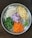A round metal tray features neatly chopped vegetables, including cauliflower, potatoes, green beans, red onions, carrots, and green chili peppers. Each type of vegetable is organized into a distinct section, showcasing a variety of colors and textures.