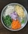 A round metal tray features neatly chopped vegetables, including cauliflower, potatoes, green beans, red onions, carrots, and green chili peppers. Each type of vegetable is organized into a distinct section, showcasing a variety of colors and textures.