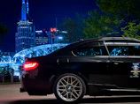 A sleek black luxury sedan parked in front of the iconic Tower Bridge at sunset.
