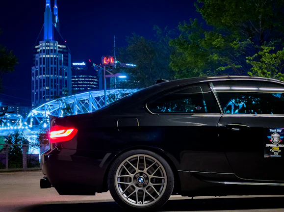 A sleek black luxury sedan parked in front of the iconic Tower Bridge at sunset.