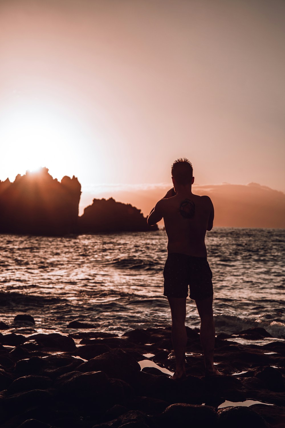 a man standing on top of a rocky beach next to the ocean