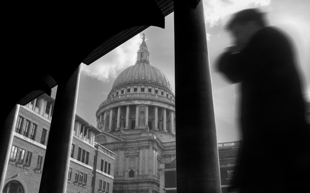 a black and white photo of a man walking in front of a building