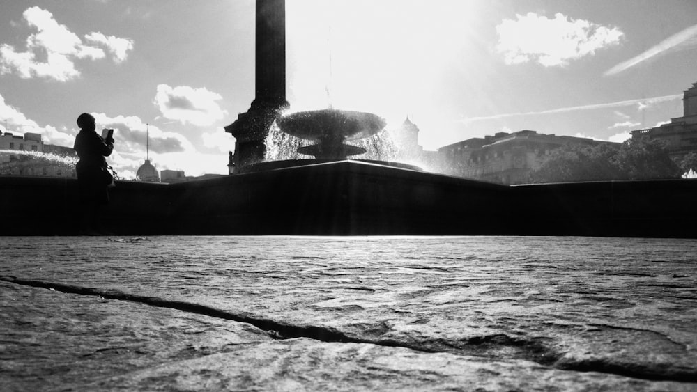 a black and white photo of a person standing in front of a fountain