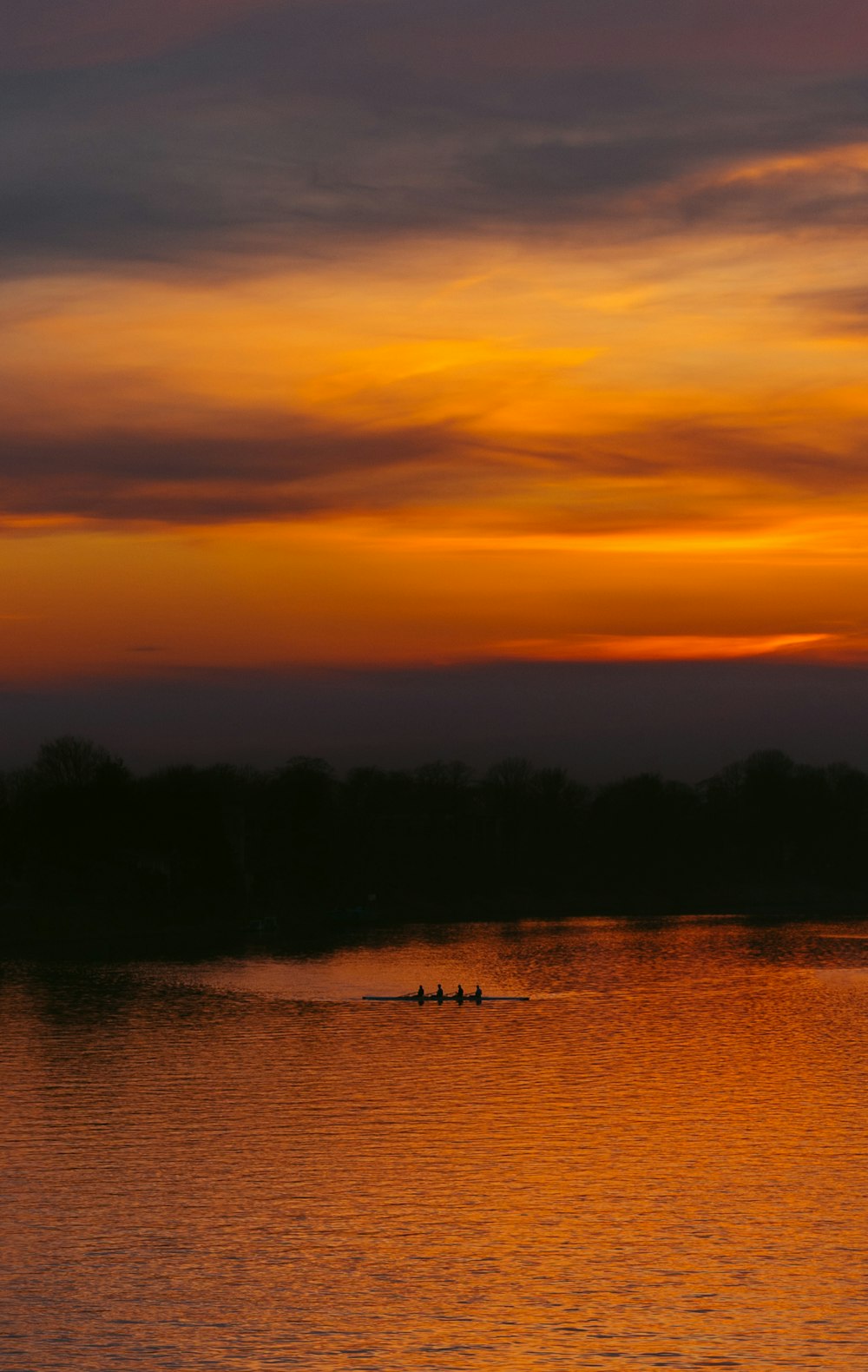 a group of people rowing a boat on a lake at sunset