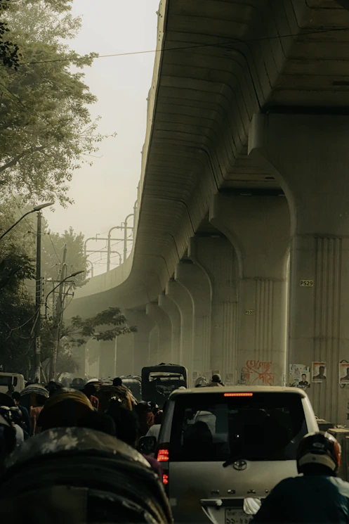 A busy city street clogged with cars emitting visible exhaust under a hazy sky.