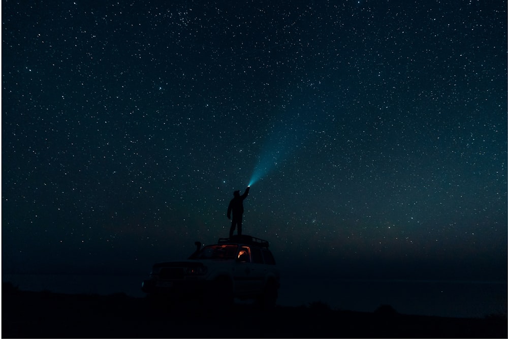 a man standing on top of a car under a night sky