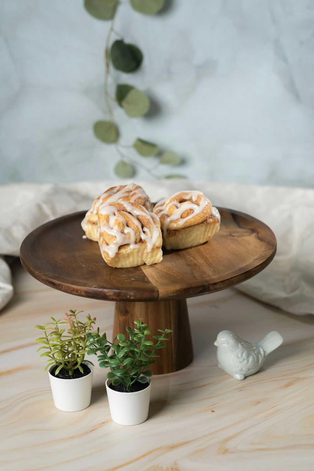 two pastries sitting on a cake stand next to a potted plant