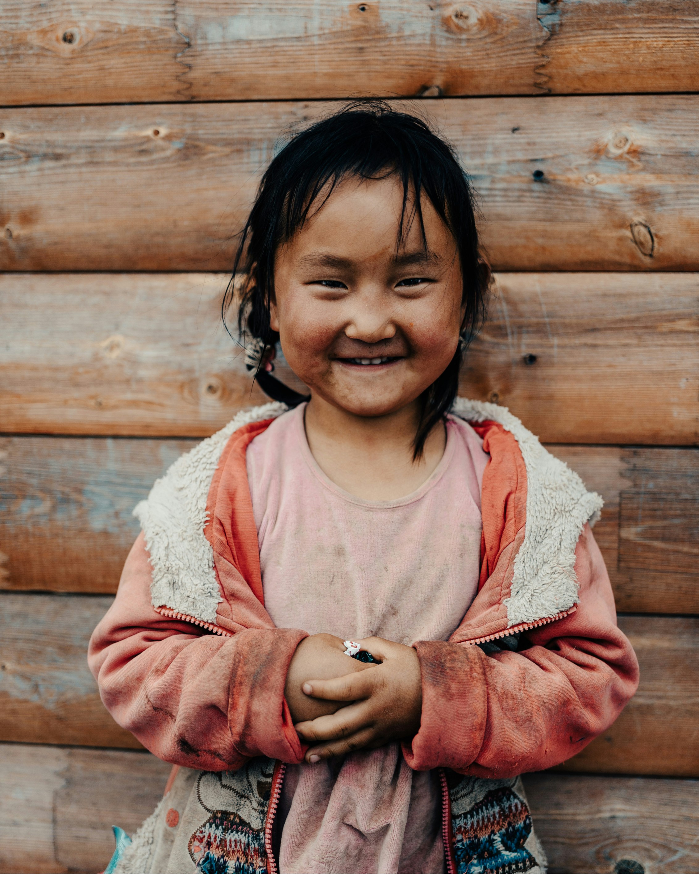 a little girl standing in front of a wooden wall