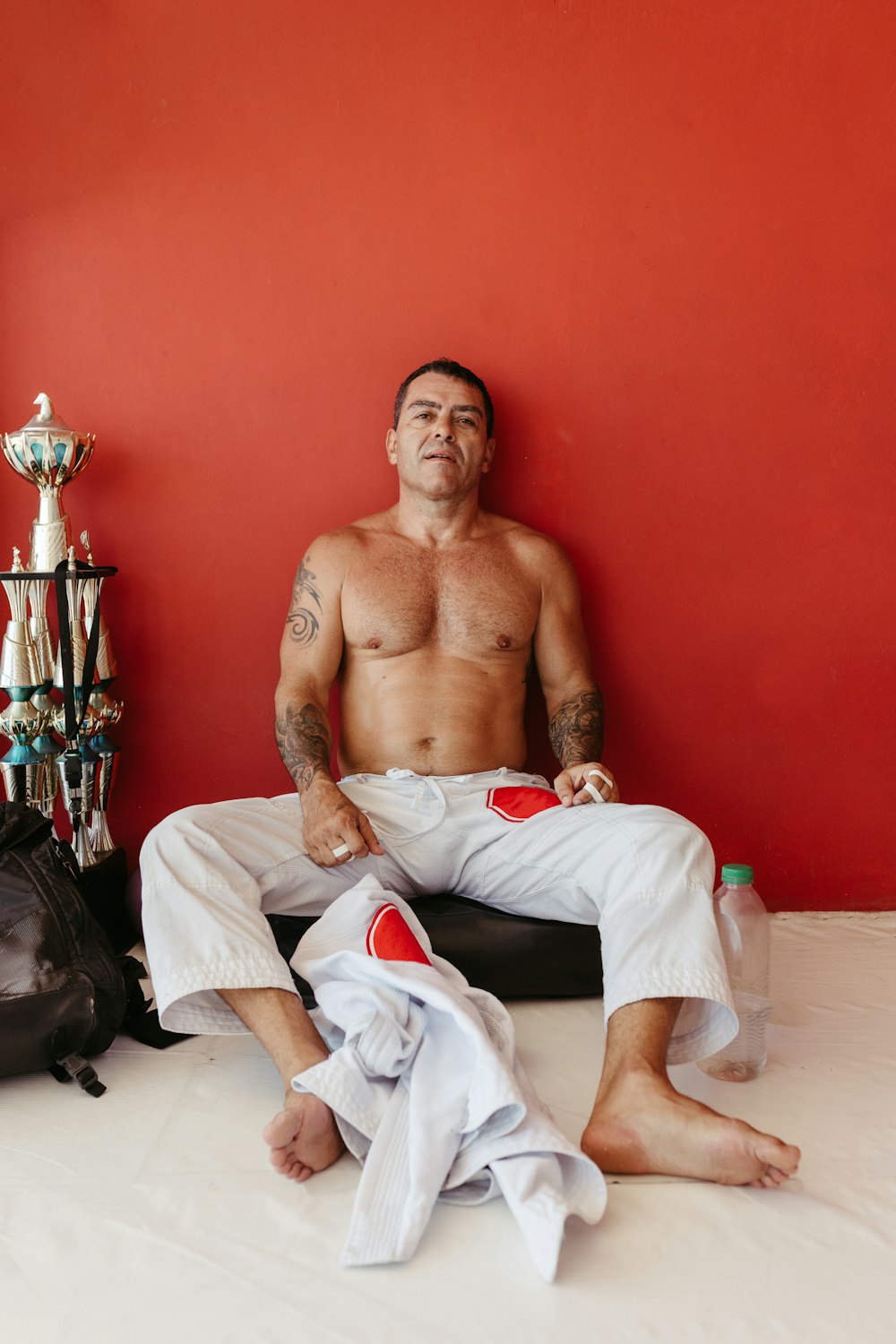 a shirtless man sitting on a bed next to a trophy