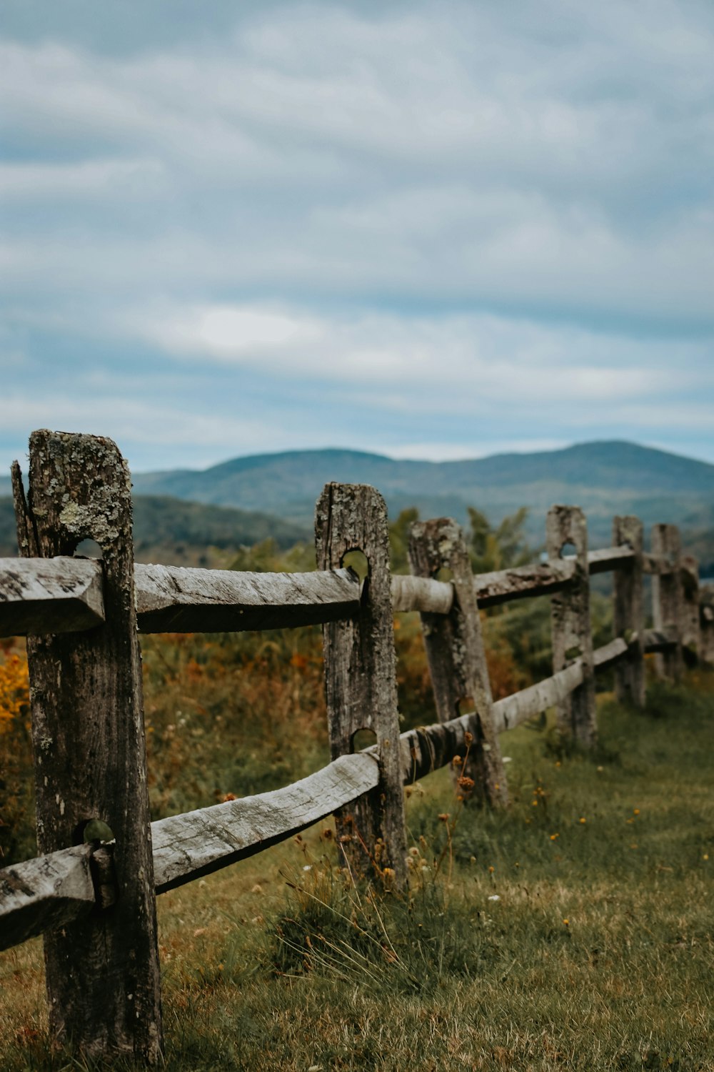 a wooden fence in a field with mountains in the background