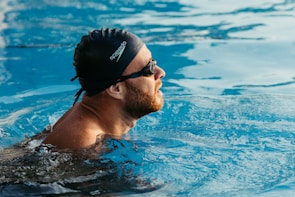 An adult swimmer adjusting a sleek black swim cap before diving into a clear pool.