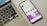 A smartphone displaying a social media profile screen with a bright purple theme, placed next to a laptop keyboard on a light-colored surface. The phone's screen shows various icons and text in French, along with profile details. The laptop's keyboard layout is visible, with black keys and white symbols.