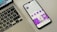 A smartphone displaying a social media profile screen with a bright purple theme, placed next to a laptop keyboard on a light-colored surface. The phone's screen shows various icons and text in French, along with profile details. The laptop's keyboard layout is visible, with black keys and white symbols.