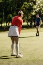 a woman in a red shirt and white skirt playing a game of golf