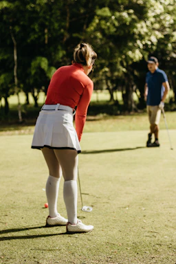 a woman in a red shirt and white skirt playing a game of golf
