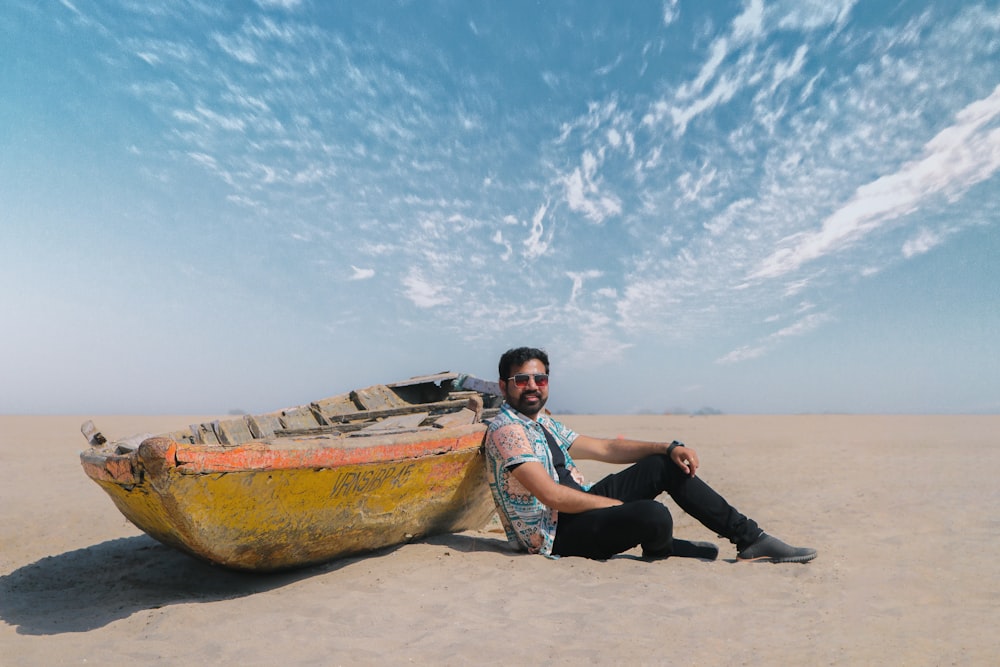 a man sitting in the sand next to a boat