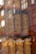 Tall, cylindrical tea containers with the label 'PALOMA TEA COMPANY' are neatly arranged on wooden shelves. The containers have a matte finish, and reflections of lights and window panes can be seen on them, adding an artistic touch.