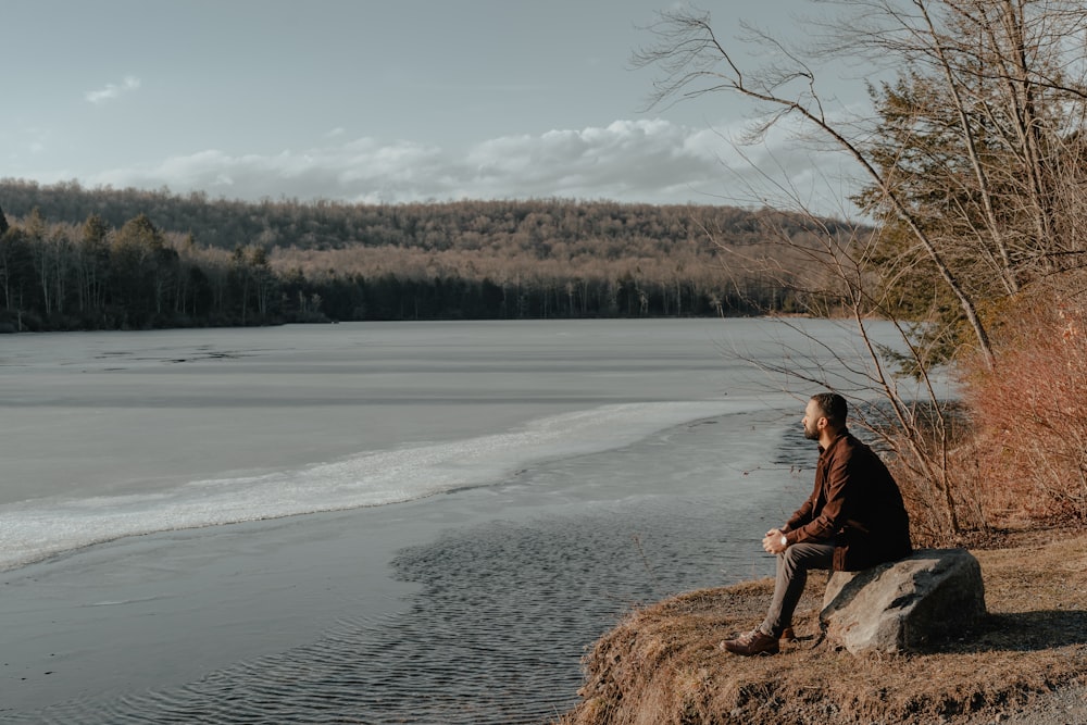 a man sitting on a rock next to a body of water