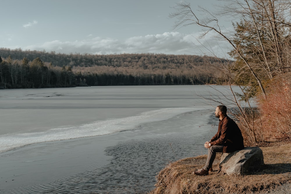 Un hombre sentado en una roca junto a un cuerpo de agua