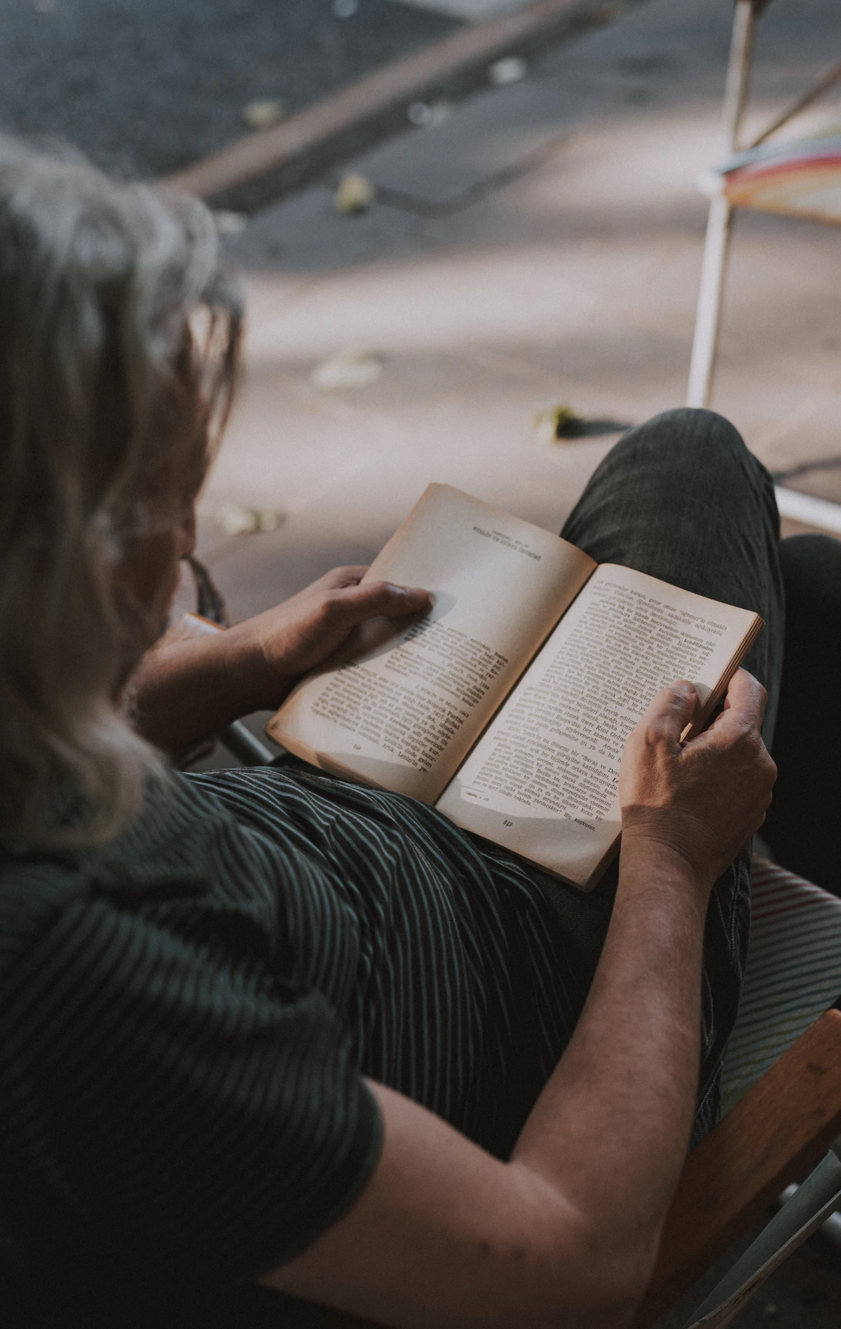 An older man reads in a chair by a window.