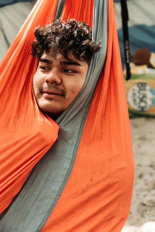 A traveler smiling while lounging in a hammock outdoors, supported by a nubevia pillow.