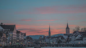 A historic city skyline at dusk, with softly glowing lights reflecting on calm river waters.