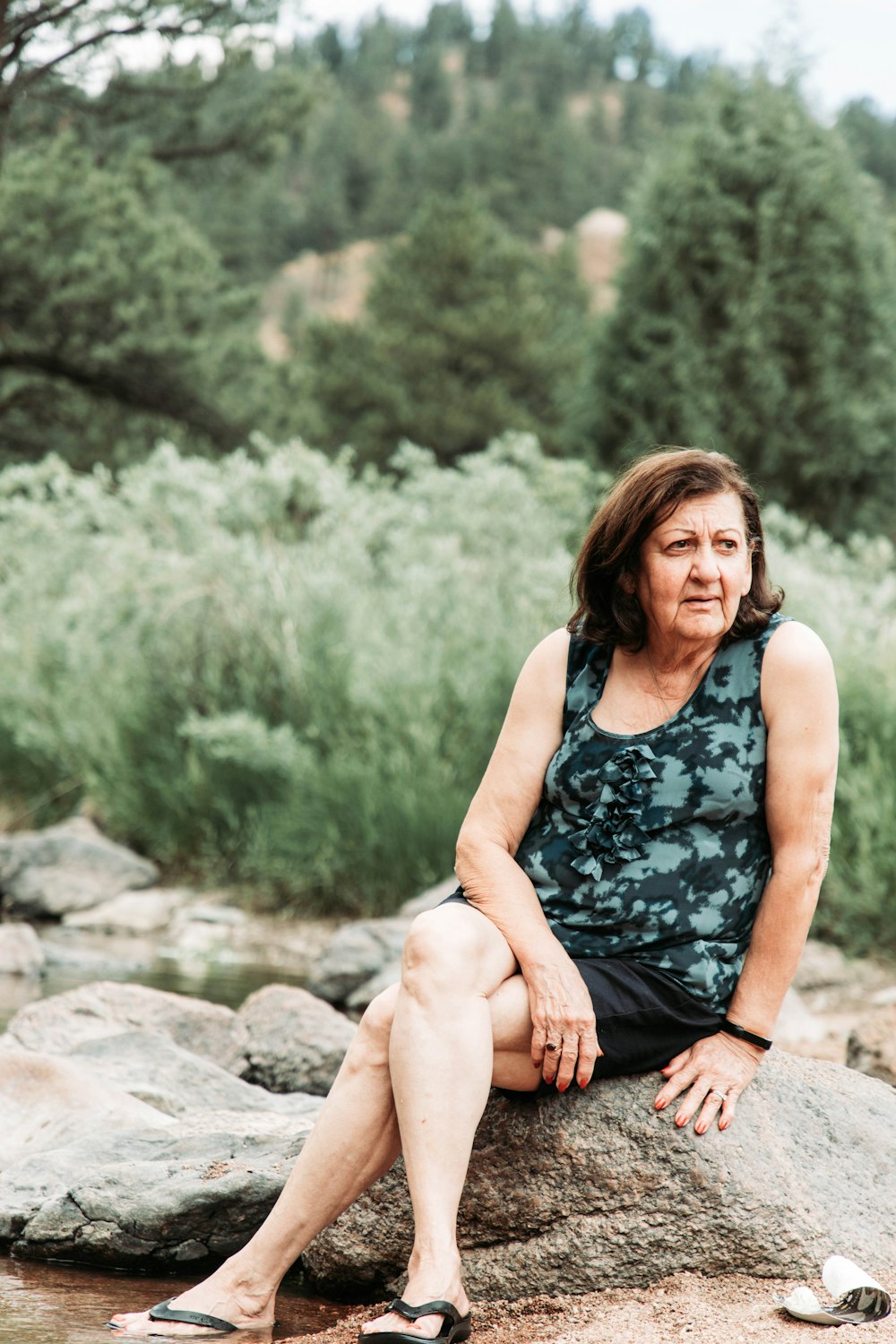 a woman sitting on top of a rock next to a river