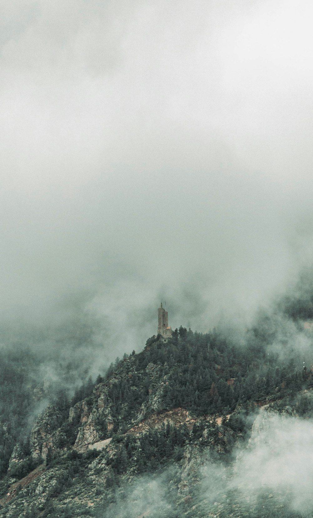 a mountain covered in fog with a clock tower in the distance