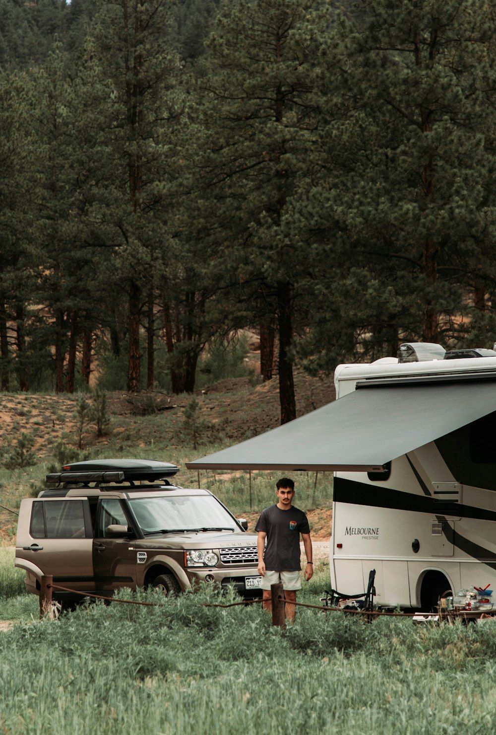 a man standing in a field next to a camper