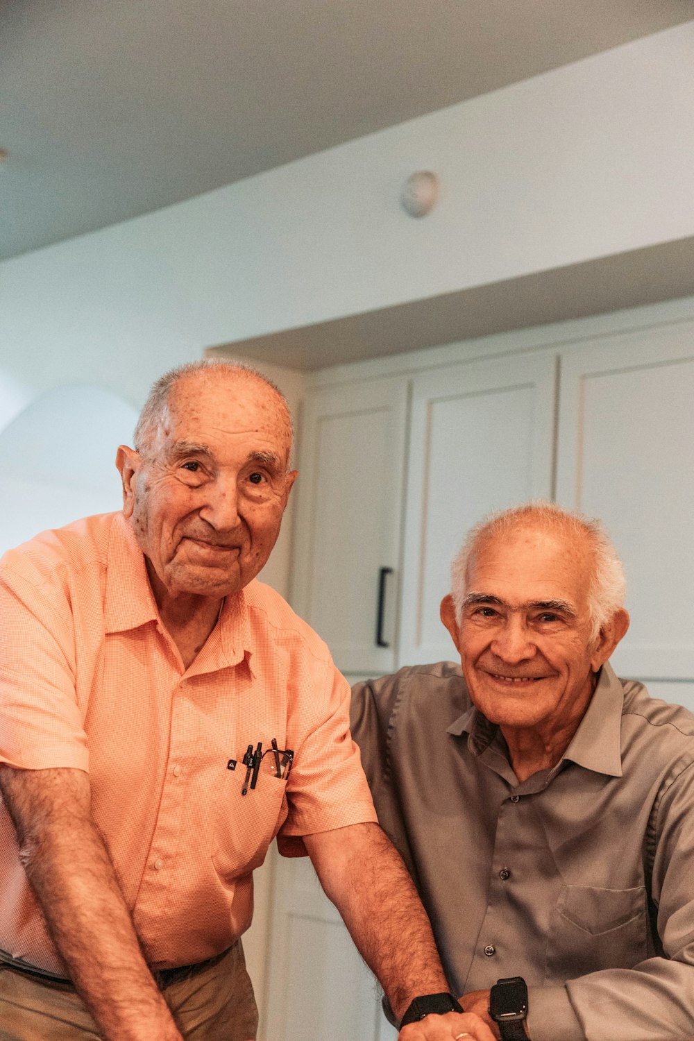 two older men sitting next to each other in a kitchen