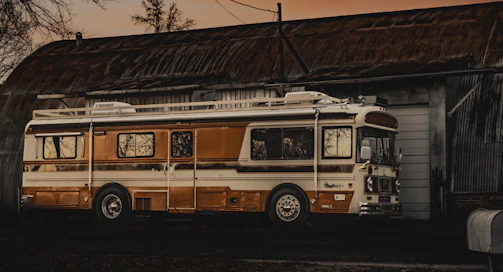 A charming vintage bus parked outside a rustic countryside venue at sunset.