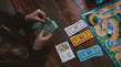 Brightly illustrated Money Villains flash cards spread out on a wooden desk with a child’s hands reaching in.