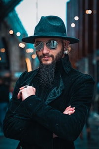 A confident man wearing sleek black Muslim attire standing against a minimalist urban backdrop.