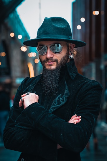 A confident man wearing sleek black Muslim attire standing against a minimalist urban backdrop.