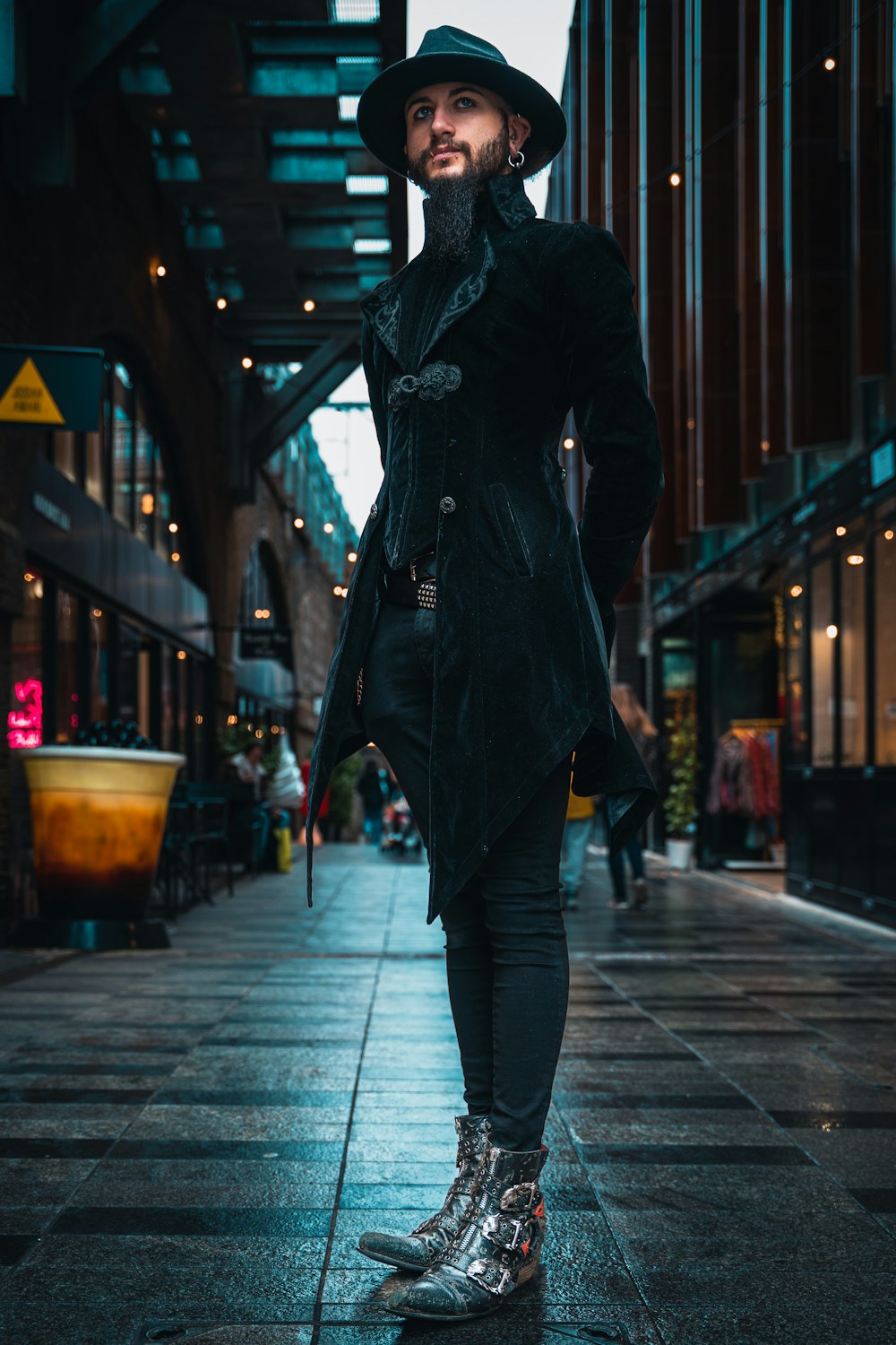 a man in a black coat and hat standing on a sidewalk