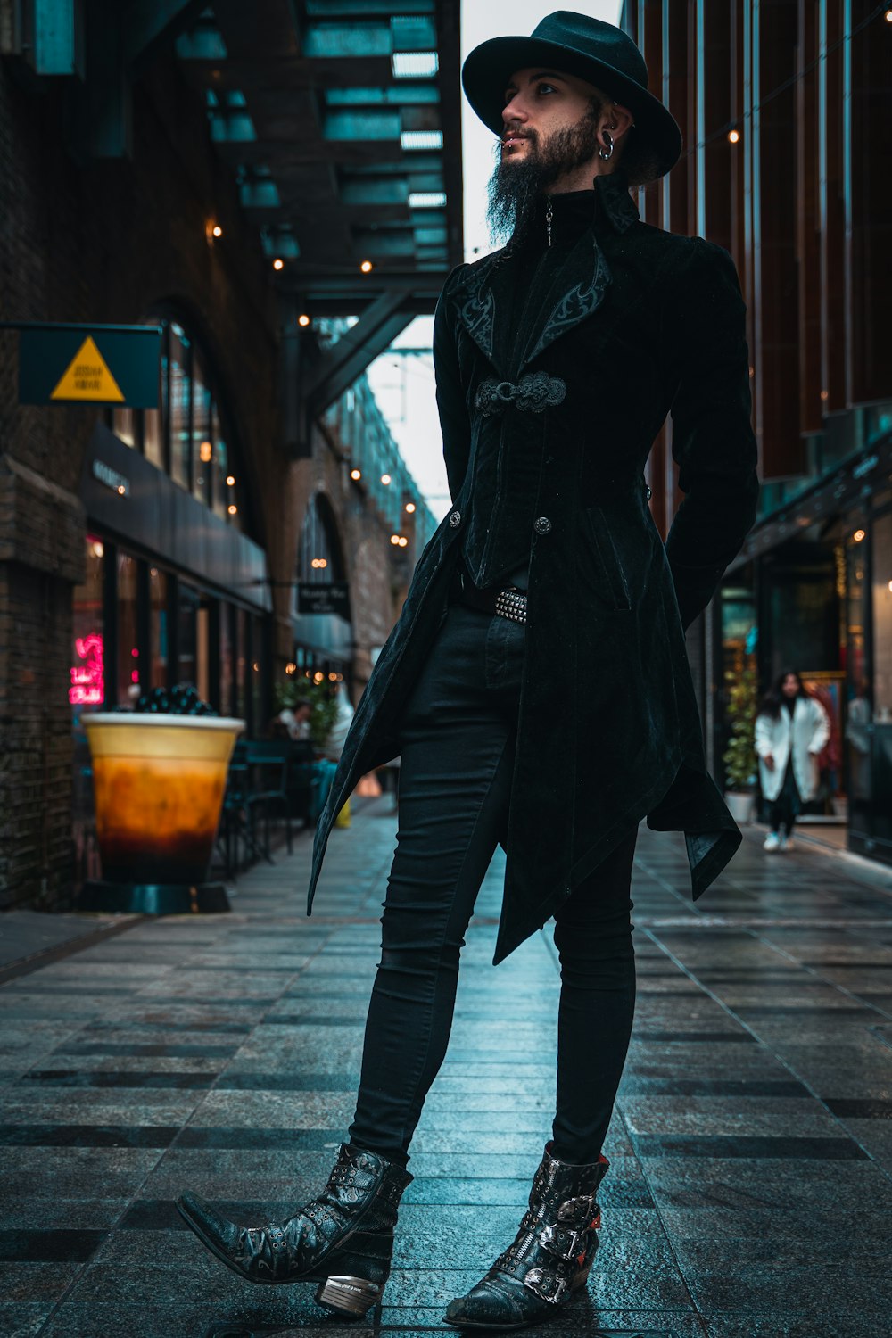 a man in a long coat and hat standing on a sidewalk